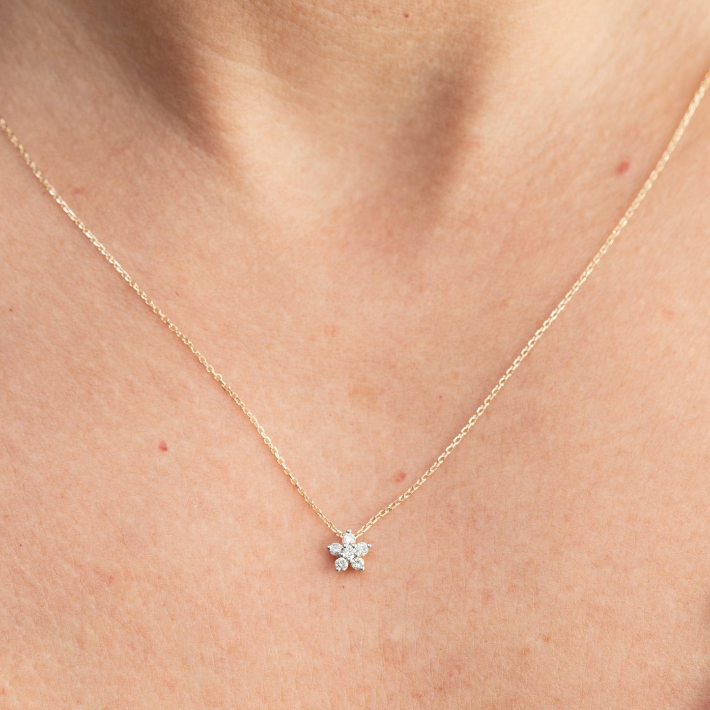 Gold necklace with a small flower pendant on a person's neck
